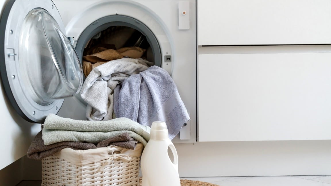 Loading a washing machine and washing clothes. A laundry basket and laundry gel in front of a household built-in washing machine in the kitchen.